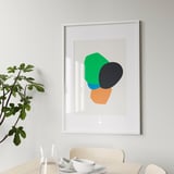 Abstracte kunst in wit kader op lichte muur boven eettafel.