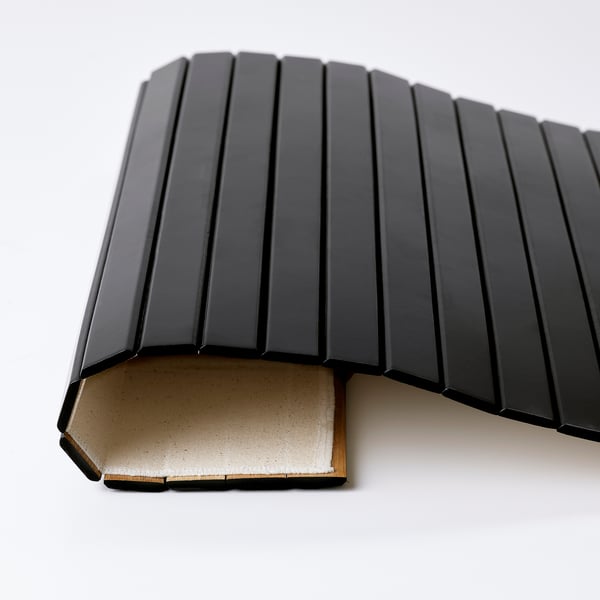 Zwart bamboe dienblad met gestructureerd oppervlak, gedeeltelijk gevouwen, rustend op een wit oppervlak.