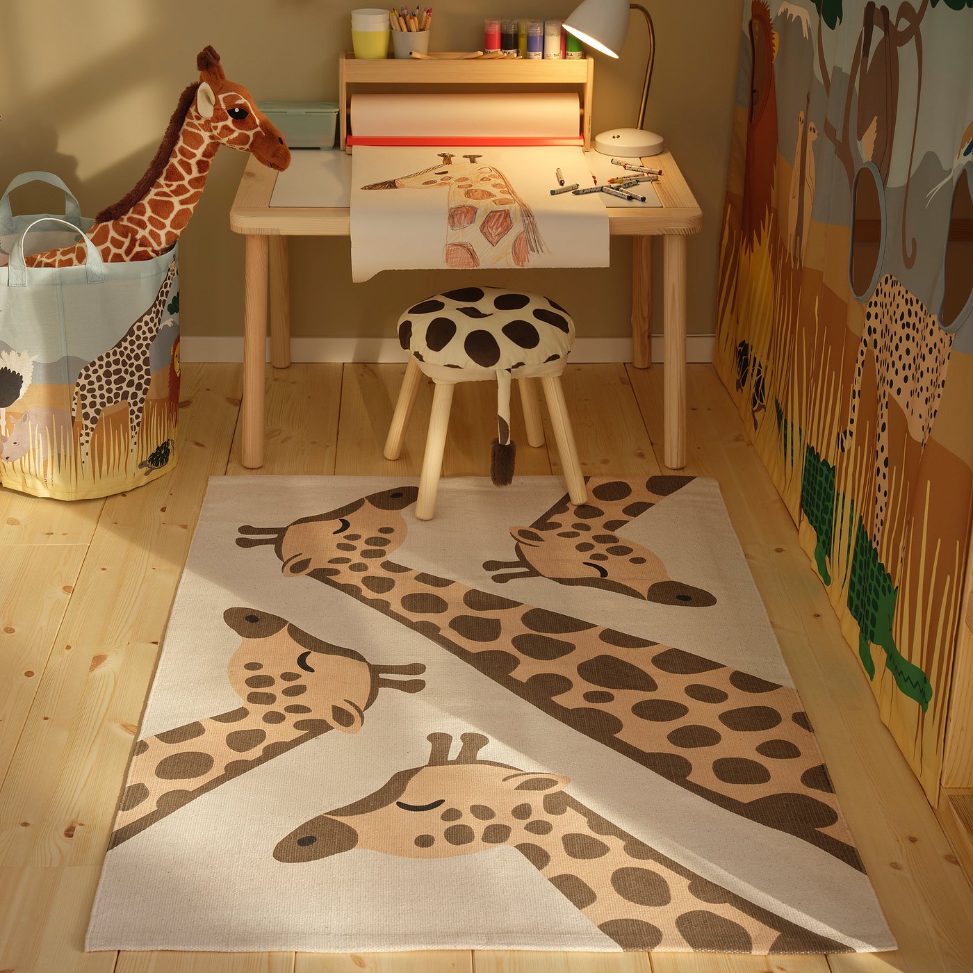 SANDLÖPARE giraffe tapijt op houten vloer, met tafel, kruk en speelgoedmand.