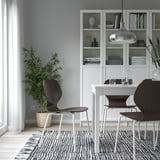 Moderne minimalistische eethoek met witte kast, donkerhouten stoelen en grote plant. Stoel: SIGTRYGG, donker hout, metalen poten.