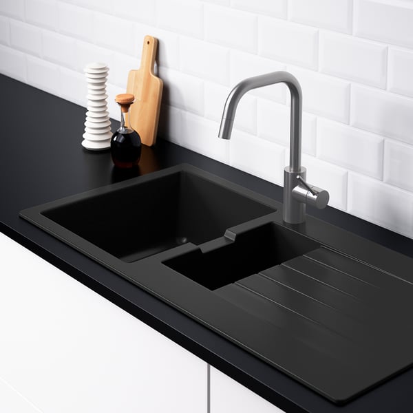 Moderne spoelbak met geïntegreerd aanrecht. Zilveren kraan, zwart aanrechtblad en wit betegelde muur.