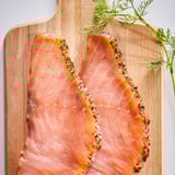 Houten snijplank met twee roze-oranje gerookte zalmfilets, gegarneerd met dille.