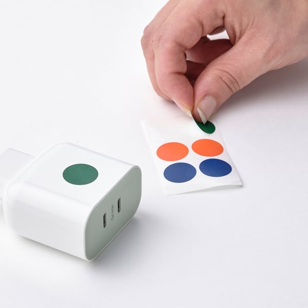 Hand plaatsen sticker op usb-c oplader. Oplader heeft groene sticker, geschikt voor meerdere apparaten.