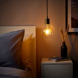 Gezellige slaapkamer met SKAFTET hanglamp boven nachtkastje. Warm getint, vernikkeld, energiezuinig ontwerp.