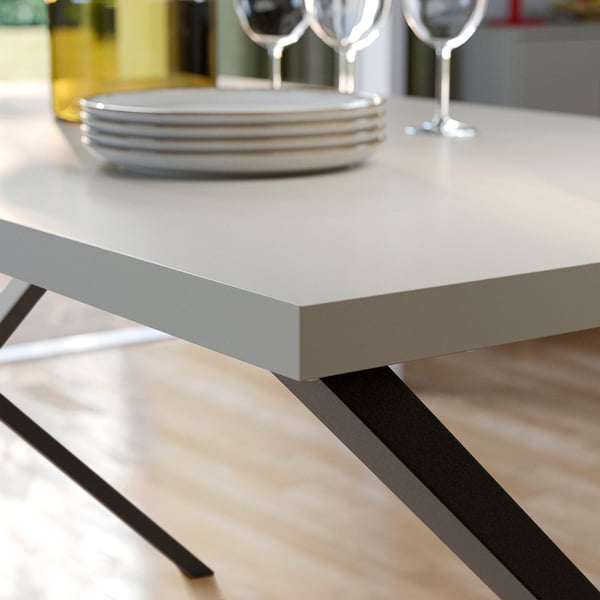 Moderne tafel met strakke, metalen randen en zwarte poten, gedekt met borden en glazen, klaar om te dineren.