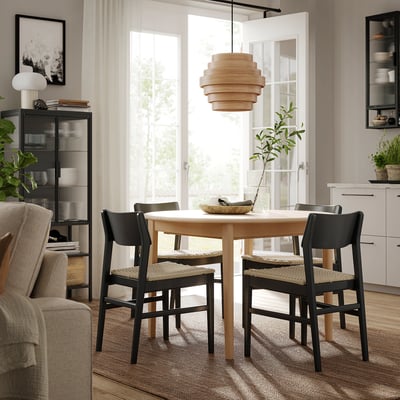 Moderne eethoek met SKANSNÄS lichthouten tafel omgeven door zwarte stoelen, unieke hanglamp, groot raam.