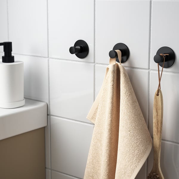 Drie zwarte haken aan betegelde muur, twee handdoeken en een hangende houten pollepel. Eenvoudig te installeren met plakband.