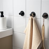 Drie zwarte haken aan betegelde muur, twee handdoeken en een hangende houten pollepel. Eenvoudig te installeren met plakband.