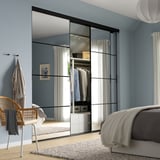 Slaapkamer met grote, lichtblauwe kastdeur voorzien van spiegelpanelen. Grijs bed, rieten stoel en hangend kledingstuk zichtbaar.
