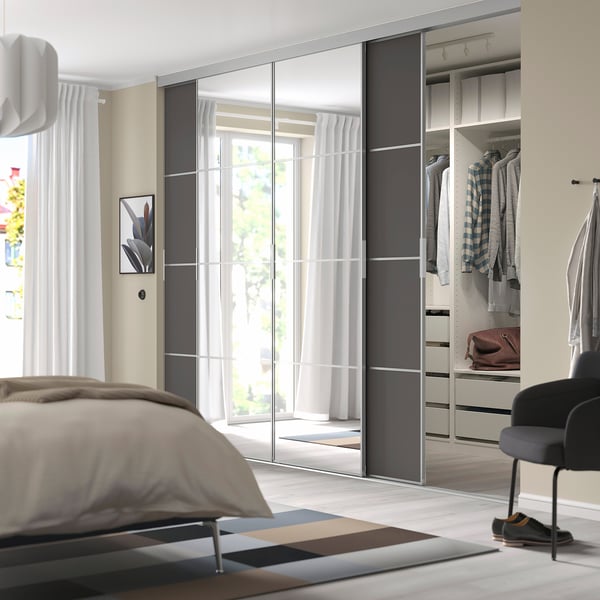 Moderne slaapkamer met SKYTTA spiegelkast, beige muren, houten vloer. Lange kledingkast met kleding, zwarte stoel. Bed met beige bekleding.