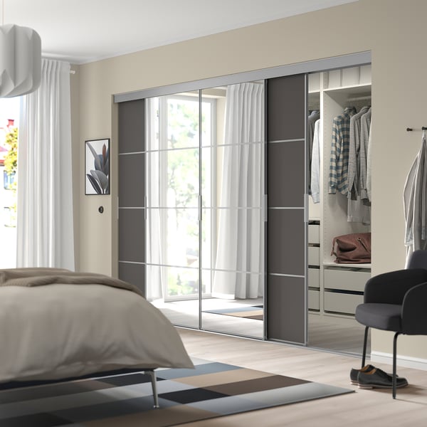 Moderne slaapkamer met grote spiegelkast, strak zilveren frame, donkergrijze panelen en glas van vloer tot plafond. Gordijnen filteren raamlicht.