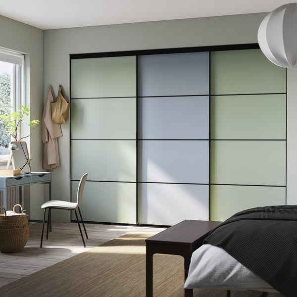 Moderne slaapkamer met grote SKYTTA kledingkast in groen-grijze tint. Schuifdeuren, houten vloer, stoel en bureau met planten.