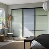 Moderne slaapkamer met grote SKYTTA kledingkast in groen-grijze tint. Schuifdeuren, houten vloer, stoel en bureau met planten.