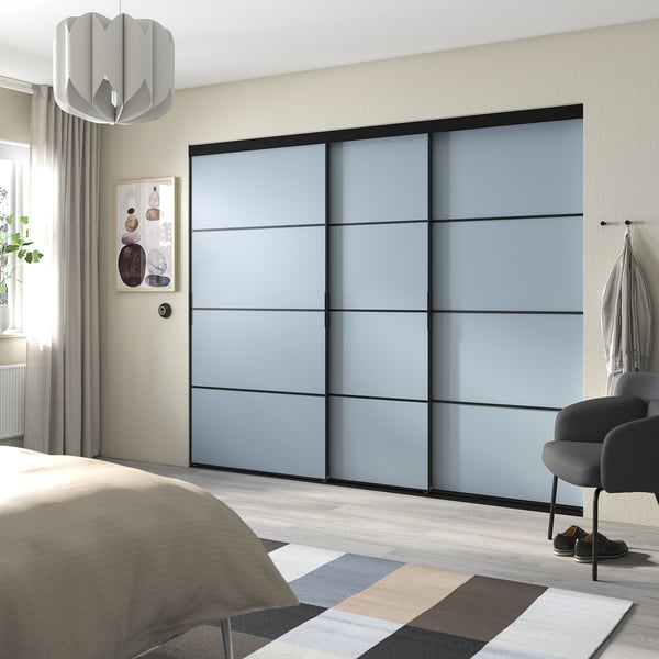 Moderne slaapkamer met blauwgrijze schuifkastdeuren, lichte houten vloer, bed met beige deken, gestreept vloerkleed en hangende lamp.
