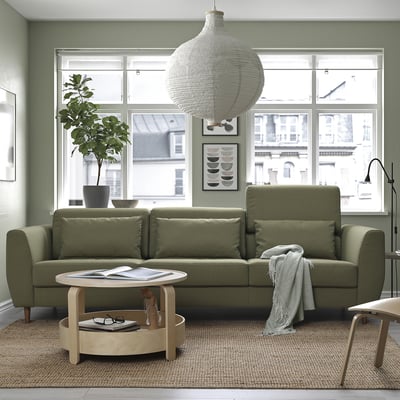 Moderne woonkamer: olijfgroene SLATORP bank, grote witte hanglamp, houten salontafel, jute vloerkleed, plant, uitzicht op de stad.