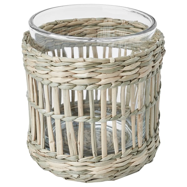 Een SLIPPRIG theelichthouder, rond, beige met rieten design. Het is gemaakt van zegge en glas.