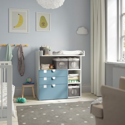 SMÅSTAD commode in de kinderkamer met blauwe lades, wieg, vloerkleed en decoraties.