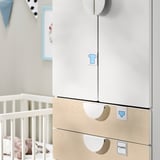 Moderne kinderkamerkast met lichthouten lades, witte deuren en soft-close scharnieren, gelegen in de buurt van een witte wieg.