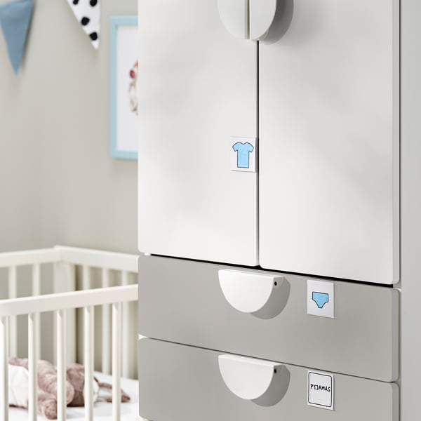 Een witte SMÅSTAD kledingkast in een kinderkamer met een wieg. Het heeft zachtsluitende scharnieren, haken en verdelers voor eenvoudige organisatie.