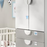 Een witte SMÅSTAD kledingkast in een kinderkamer met een wieg. Het heeft zachtsluitende scharnieren, haken en verdelers voor eenvoudige organisatie.