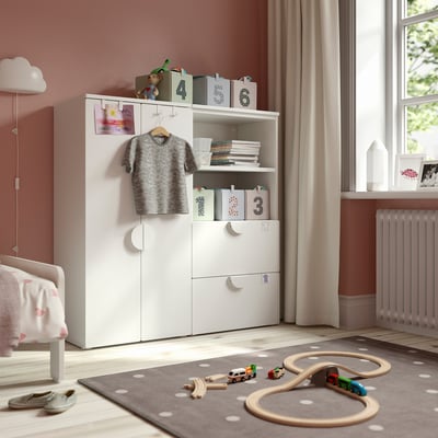 Een kinderkamer met een witte SMÅSTAD opbergkast. Het heeft planken, lades en een kledingroede. De kamer een bed, speelgoed en een raam.