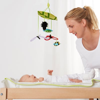 Blonde vrouw glimlachen bij baby op commode, naast kleurrijke mobiel.