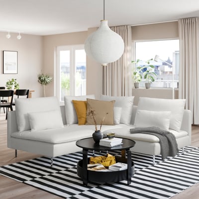 Moderne woonkamer met SÖDERHAMN bank, houten vloer, gestreept vloerkleed, salontafel met boeken en groot raam met beige gordijnen.