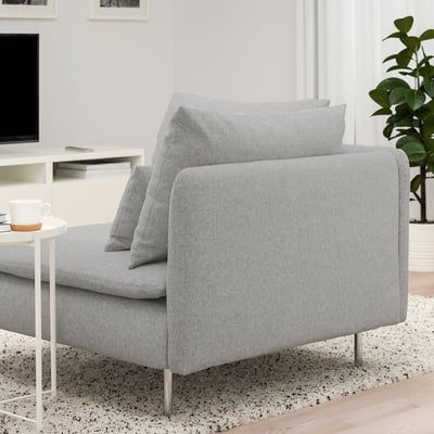 Een moderne, lichtgrijze bank met kussens op een gespikkeld vloerkleed. De bank is ontworpen met hoge poten en diepe zittingen voor comfort.