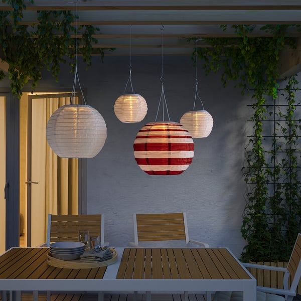 Vier SOLVINDEN lantaarns in rood, wit en andere kleuren verlichten een eethoek buiten onder een pergola.