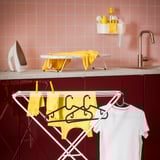 Gele en witte kleren drogen op metalen hanger in wasruimte met roze tegels.
