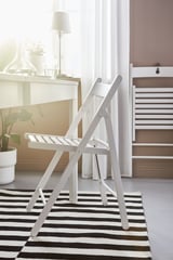 Witte klapstoelen op zwart-wit gestreept tapijt in de buurt van raam met lamp en plant.