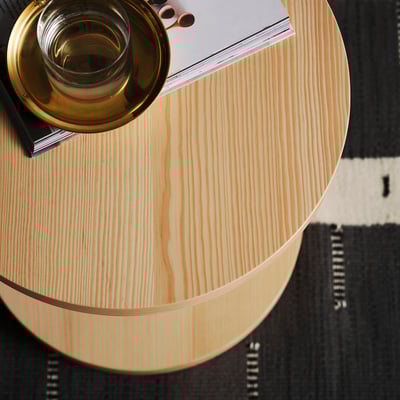 Bovenaanzicht van minimalistisch, licht houten STOCKHOLM 2025 bijzettafel met messing beker, zwart boek, op tapijt met patroon.