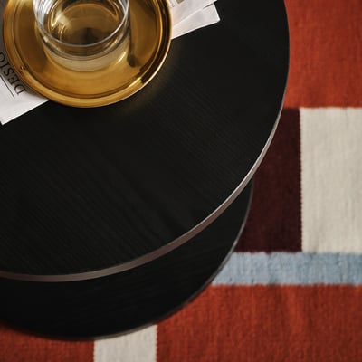 Zwarte ronde bijzettafel, enkele poot, veelkleurig vloerkleed, gouden dienblad, glas