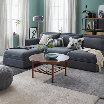 Gezellige woonkamer met groot grijs STOENSE vloerkleed, sectionele bank, houten salontafel en groene wanden.