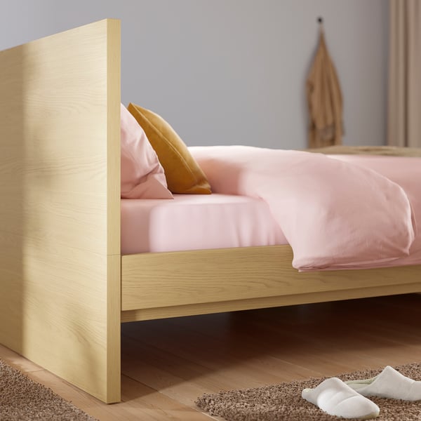 Houten bed met roze beddengoed, hoog hoofdeinde, houten vloer.