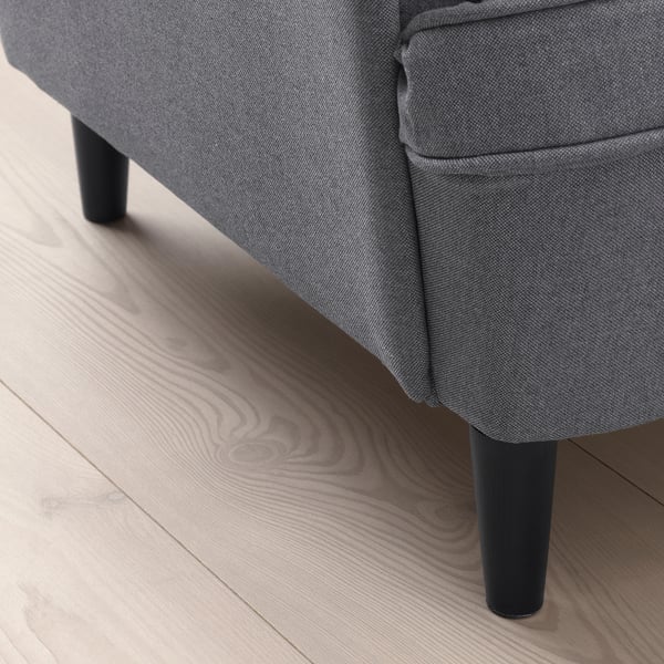 Close-up van een grijze STRANDMON kinderfauteuil met zachte, duurzame stof en stevige zwarte poten op een houten vloer.