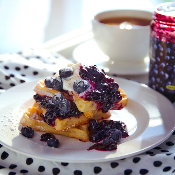 Een bord wafels belegd met bosbessenjam en verse blauwe bessen, vergezeld van een kopje koffie.