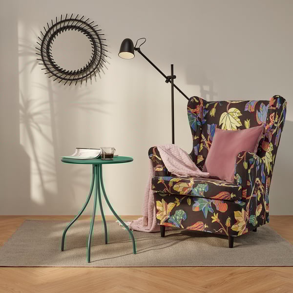 Donkergroene TÅNEBRO bijzettafel met slanke poten naast een fauteuil met patroon.