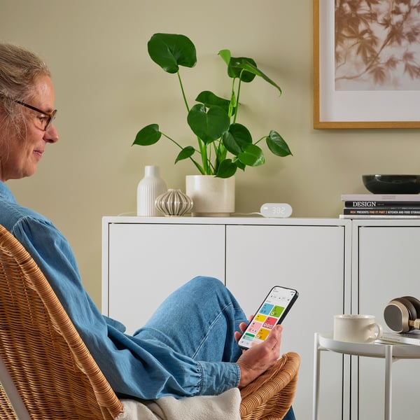 Persoon die op een stoel zit met een smartphone; De temperatuur van de TIMMERFLOTTE-sensor op kastdisplays.