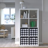 Witte TJENA doos met zwarte stippen op plank tussen boeken en decor.