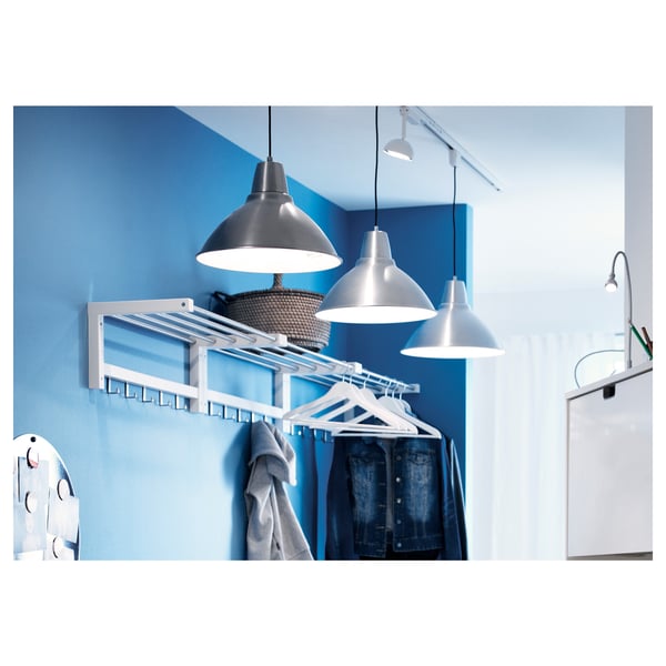 Blauw TJUSIG rek aan de muur voor kleding & mand met trui. Twee zilveren hanglampen en een groen gearceerde witte lamp.