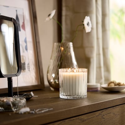 Houten tafel met brandende TOFSTÄRNA-kaars , glazen vaas met bloem, sieraden en spiegel.