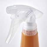 Doorzichtige sproeikop op oranje fles. Instelbare spuitinstelling, transparante trekker, stevig op de fles bevestigd.