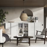 Moderne woonkamer met TONSTAD gebroken witte kast, ronde houten tafel, stoelen en stijlvolle verlichting.