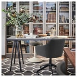 Opstelling thuiskantoorbureau: modern bureau, grijze stoel, glazen vaas met bloemen, boekenplanken.