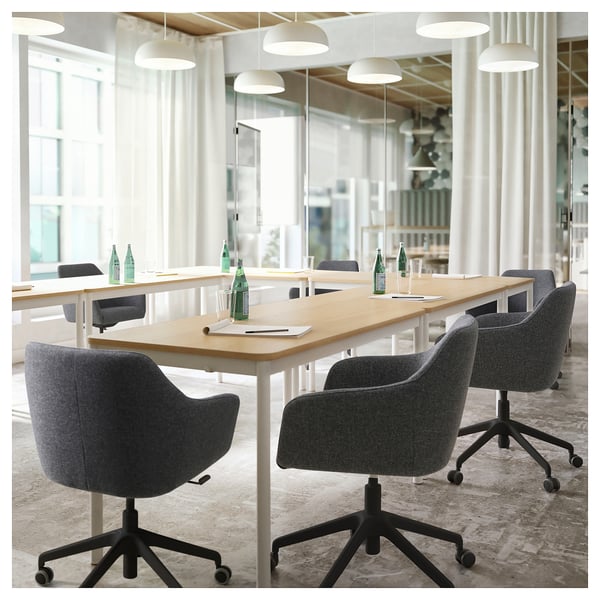 Moderne vergaderruimte met TOSSBERG draaistoelen in grijze stof, lange houten tafel, groene waterflessen en hanglampen.