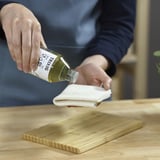 Persoon giet vloeistof uit de TRIXIG-fles op een witte doek in de buurt van een houten snijplank.
