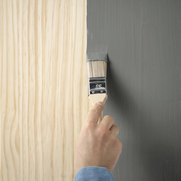 Een hand die een houten oppervlak met grijze semi-matte verf schildert met behulp van een penseel.