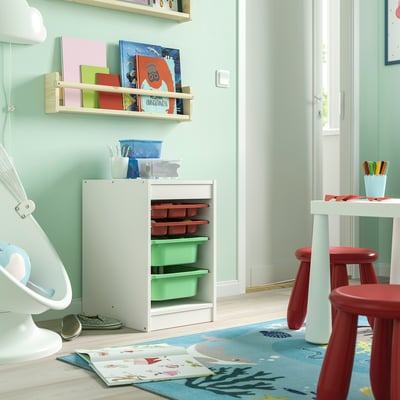 Kinderspeelkamer met TROFAST wit opbergmeubel, rode krukken, boeken en kleurrijk vloerkleed.