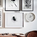 Wanddecoratielijsten en een witte klok. Het wijzerplaat van de klok toont getallen als punten, zwarte wijzers tonen tijd aan. Daaronder staan kleine kommen op een gevlochten mand en tafel.
